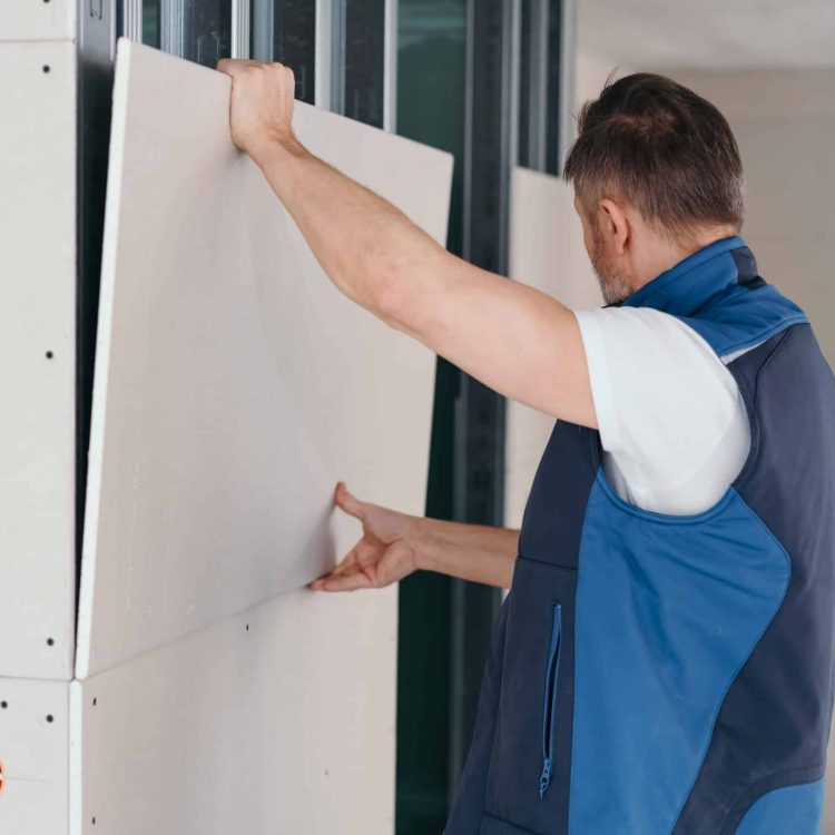 Builder fitting white wood cladding in a new build house with open electrical sockets visible below